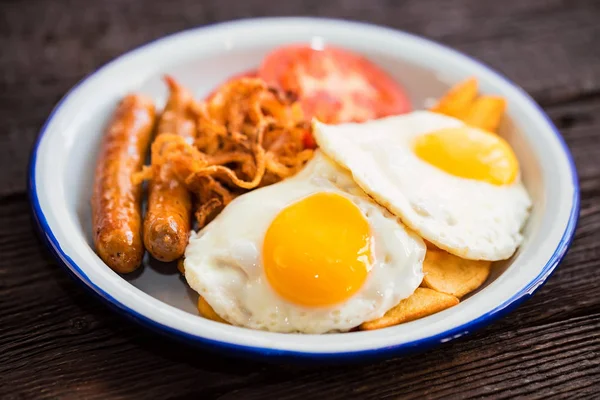 Типовой завтрак с яйцами, помидорами, луковыми кольцами и колбасой на тарелке — стоковое фото
