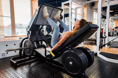 Genç sportif kadın bacak basın makinesi üzerinde bacak egzersizleri yapar
