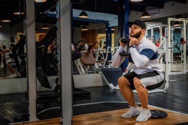 Genç adam spor salonunda statik veya izometrik çömelme yapıyor.