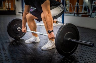 Genç formda adam modern spor salonunda kaldırma yapıyor.