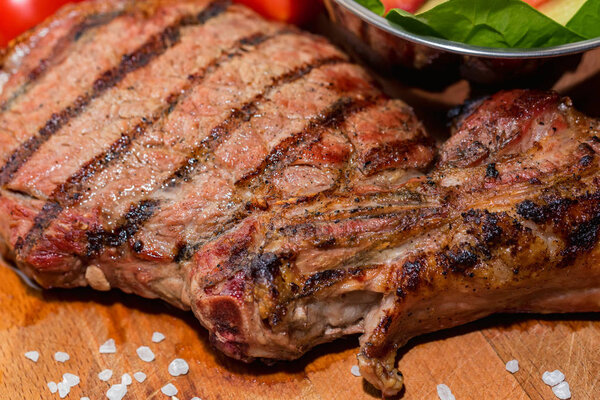 Delicious grilled bone steak on wooden background with tomatoes and fresh vegetable salad in chrome bowl. Selective focus
