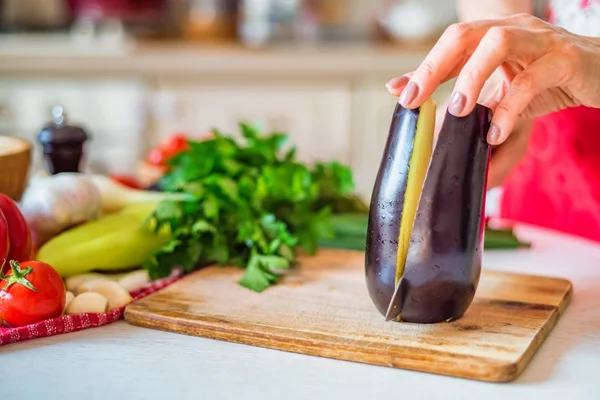 Женская рука с ножевыми порезами баклажанов на кухне. Кулинария — стоковое фото