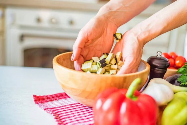 Female hand put cut eggplant in wooden bowl in kitchen. Cooking vegetables — Stock Photo, Image