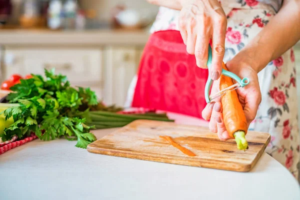 Female hand with peels carrot in kitchen. Cooking vegetables — Stock Photo, Image
