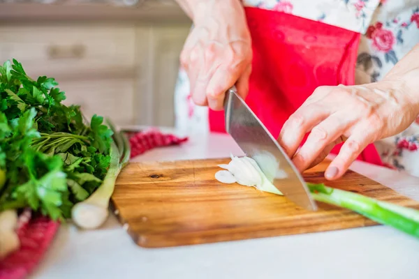 Female hand with knife cuts green leek in kitchen. Cooking vegetables — Stock Photo, Image