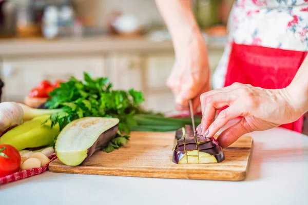 Female hand with knife cuts eggplant on board in kitchen. Cooking vegetables — Stock Photo, Image