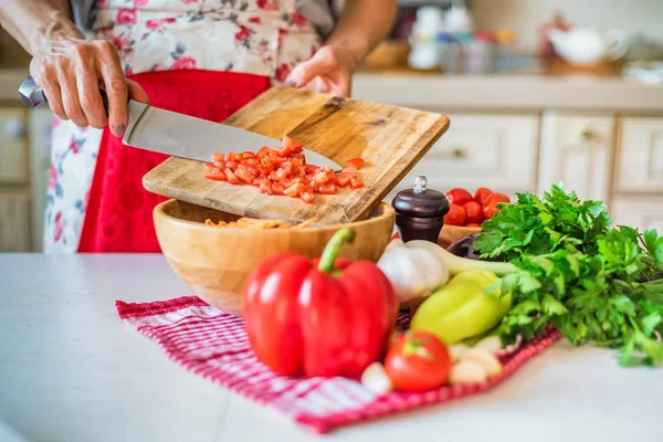 Female hand put chopped tomato in wooden bowl in kitchen. Cooking vegetables — Stock Photo, Image