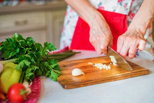 Female hand with knife chops garlic in kitchen. Cooking vegetables — Stock Photo, Image
