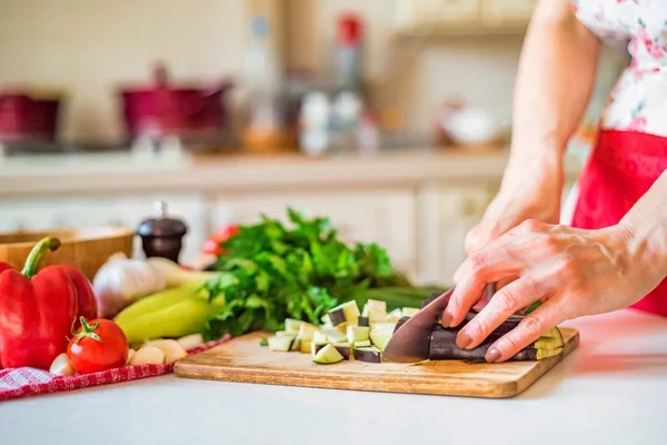 Close up female hand with knife cuts eggplant on wooden board in kitchen — Stock Photo, Image