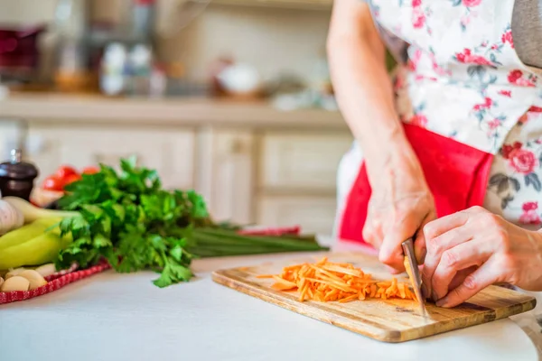 Female hand with knife chops carrot in kitchen. Cooking vegetables — Stock Photo, Image