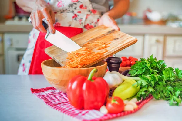 Female hand put chopped carrot in wooden bowl in kitchen. Cooking vegetables — Stock Photo, Image