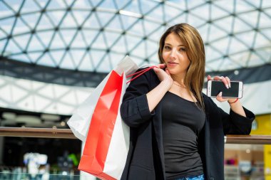 Bulanık alışveriş merkezinde alışveriş çantaları ve telefon ile beatiful kahverengi saçlı kız
