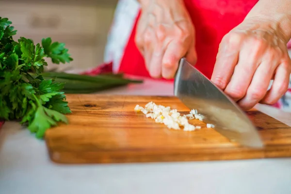 Female hand with knife chops garlic in kitchen. Cooking vegetables — Stock Photo, Image