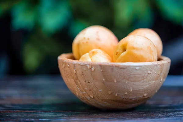 Fresh ripe apricots in wooden bowl outdoors. Blurred background — Stock Photo, Image