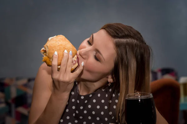 Jonge vrouw eten hamburger in restaurant. Close-up gezicht met gesloten ogen — Stockfoto