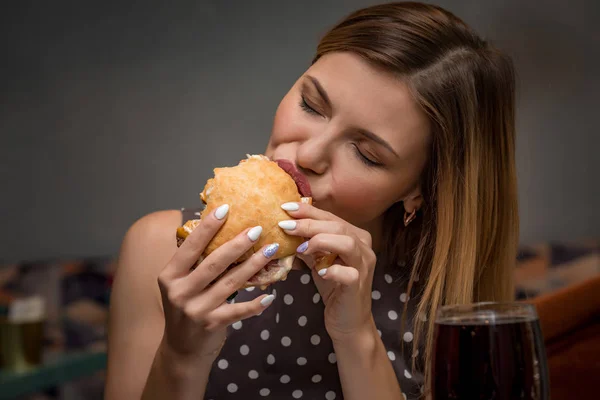 Jonge vrouw eten hamburger in restaurant. Close-up gezicht met gesloten ogen — Stockfoto