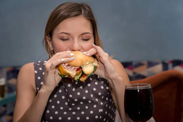 Mujer joven comiendo hamburguesa en el restaurante. Cara cerrada con los ojos cerrados — Foto de Stock