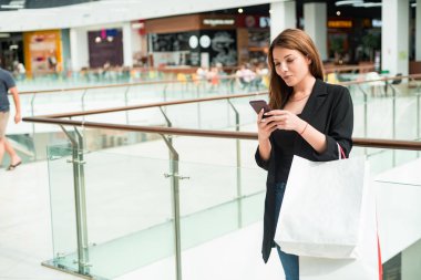 Alışveriş poşetleri ile güzel kahverengi saçlı kız alışveriş merkezinde telefon kullanır