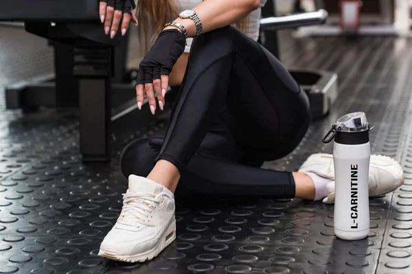 Çekici model modern spor salonunda L-carnitine içeceğiyle oturur. Alt kısım görünümü
