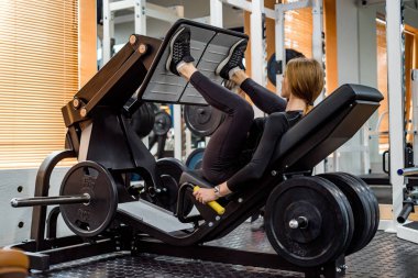 Genç sportif kadın bacak basın makinesi üzerinde bacak egzersizleri yapar