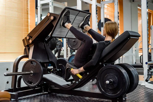 Unga sportig kvinna gör ben övningar på benet press maskin — Stockfoto