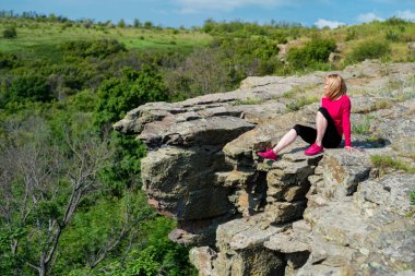 Kadın yürüyüşçü yaz aylarında kaya kenarında oturur