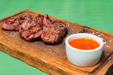 Ahşap bir mutfak tahtasına sosla süslenmiş ızgara sığır eti madalyonu.