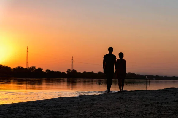 Silhouette of two children walking on the river bank at sunset Stock Picture