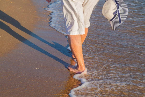 Legs of an elderly woman. Walk along the beach along the coast.