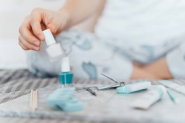 Coronavirüs salgını yüzünden tırnak cilasıyla manikür yapan genç bir kadın. Karantina ya da kendini izole etme süresince ev hayatı, yeni normal kavram. Seçici odak.