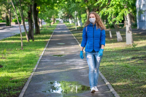 A Caucasian blond woman in a protective mask and gloves is walking on empty the street. Prevention of viral infection. Responsible social behavior of a citizen in a public place. Copy space