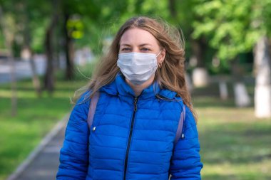 Beyaz, koruyucu maskeli ve eldivenli sarışın kadın boş cadde boyunca yürüyor. Koronavirüs salgını sırasında yaşam tarzı ve güvenli davranışlar. Yeni normal ve modern gerçeklik 2020. Güvenlik önlemleri