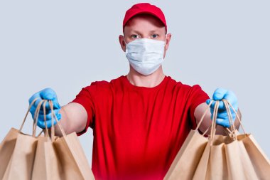 Güvenli teslimat. Kırmızı üniformalı, koruyucu maskeli ve eldivenli bir kurye büyük bir sipariş, bir sürü kese kağıdı ve karantinaya konulamaz yiyecek taşır. Gönüllü bağışı. Sıfır atık