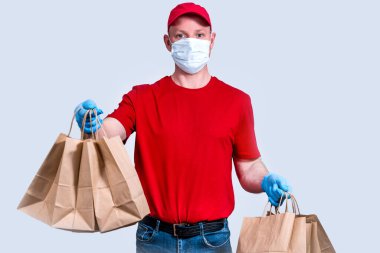 Güvenli teslimat. Kırmızı üniformalı, koruyucu maskeli ve eldivenli bir kurye büyük bir sipariş, bir sürü kese kağıdı ve karantinaya konulamaz yiyecek taşır. Gönüllü bağışı. Sıfır atık