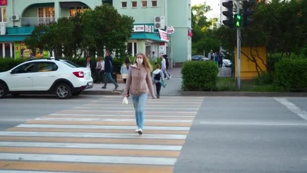 Blond caucasien dans un masque de protection traverse la route dans le centre de la ville. Protection contre le coronavirus dans un lieu public. Le style de vie après une pandémie. Russie, Volgodonsk 25 juin 2020. — Video