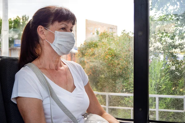 Mulher adulta com uma máscara protetora cavalga sozinha em um vazio no transporte público na cidade. Distância social. Os passageiros do autocarro estão protegidos do coronavírus. Novo normal. estilo de vida durante a pandemia — Fotografia de Stock