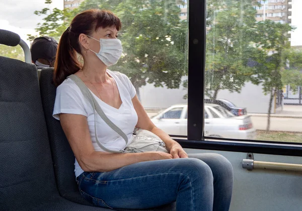 Mulher adulta com uma máscara protetora cavalga sozinha em um vazio no transporte público na cidade. Distância social. Os passageiros do autocarro estão protegidos do coronavírus. Novo normal. estilo de vida durante a pandemia — Fotografia de Stock