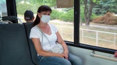Koruyucu maskeli yetişkin bir kadın şehirde boş bir toplu taşıma aracında tek başına geziyor. Sosyal mesafe. Otobüs yolcuları koronavirüsten korunuyor. Yeni normal. Salgın sırasında yaşam biçimi