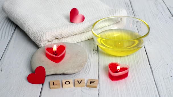 Le concept d'un Spa pour la Saint-Valentin. Brûlez des bougies rouges en forme de cœur, des pierres, de l'huile de massage, du mot amour et une serviette blanche sur un fond en bois. Soins de relaxation et de bien-être. Procédure de bain, cosmétologie — Video