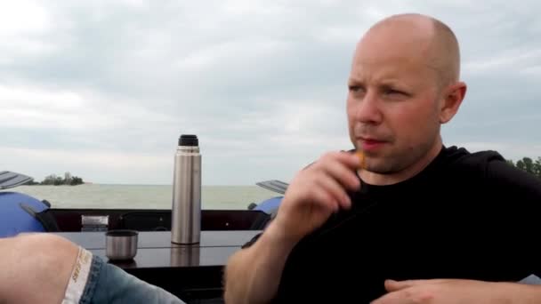 Le pêcheur flotte sur la rivière dans un bateau en caoutchouc. Un homme se repose, oscille sur les vagues, boit le thé du thermos et se détend. Activités de plein air, excursions en bateau d'été et pêche. Russie, Volgodonsk : 14 juillet 2020. — Video