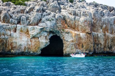 Arka planda turistler olan küçük turist motorlu teknesi. Akdeniz dağlarındaki büyük bir mağaraya giriş. Antalya vilayetinin çevresindeki turda. Kemer, Türkiye 11 Haziran 2018.