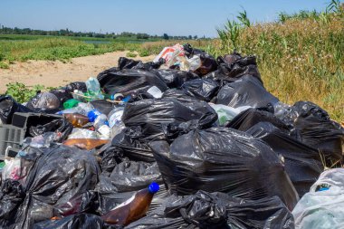 Nehir kıyısına dök. Doğadaki çöpler. Bir sürü siyah çöp torbası. Çevresel kirlilik sorunu. Büyük bir şehirde katı atık imhası. Volgodonsk, Rusya 07 Mart 2020.
