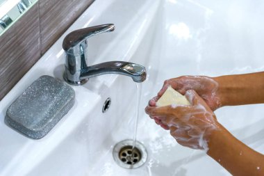 Genç bir kız ellerini lavabodaki bir su deresinin altında sabun köpüğüyle yıkıyor. Bakteri ve viral enfeksiyonun yayılmasını önlemek için temiz eller. Salgın sırasında korunma. Temizlik ve temizlik..