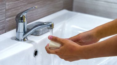Pankart. Kız ellerini lavabodaki bir su deresinin altında sabun köpüğüyle yıkıyor. Bakteri ve viral enfeksiyonun yayılmasını önlemek için temiz eller. Salgın sırasında korunma. Temizlik ve temizlik..