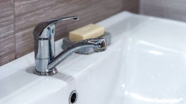 Pankart. İç kısımda beyaz lavabo ve modern metal ekonomik su musluğu var. Su tasarrufu. El yıkama ve hijyen için sabun. Bakteri ve viral enfeksiyonun yayılmasını önler. Boşluğu kopyala.