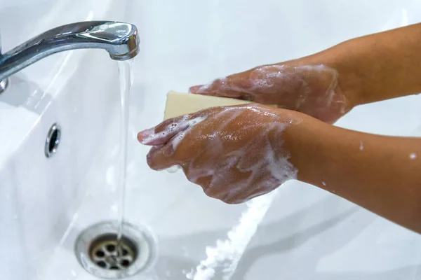 A teenage girl washes her hands in soap suds under a stream of water in sink. Clean hands to prevent the spread of bacteria and viral infection. Protection during a pandemic. Hygiene and cleanliness. — Stock Photo, Image