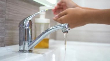 Ergen ellerini lavabodaki bir su deresinin altında sabunla yıkıyor. Bakteri ve virüs bulaşmasını önlemek için ellerinizi temizleyin. Bir salgın sırasında çocukları korumak. Temizlik ve temizlik..