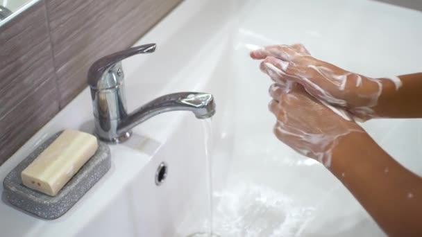 Tiener wast zorgvuldig zijn handen met overvloedige zeeppeulen onder een stroom water in de gootsteen. Reinig uw handen om verspreiding van bacteriën en virale infectie te voorkomen. Bescherming van kinderen tijdens een pandemie. — Stockvideo