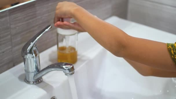 Um menino pequeno abre a torneira e lava as mãos com sabão em água corrente no lavatório. Limpe as mãos para evitar a propagação de bactérias e infecções virais. Proteger as crianças durante uma pandemia. — Vídeo de Stock