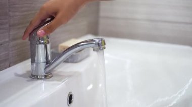 Genç bir çocuk musluğu açar ve lavaboda akan suyun altında ellerini sabunla yıkar. Bakteri ve viral enfeksiyonun yayılmasını önlemek için ellerinizi temizleyin. Bir salgın sırasında çocukları korumak.